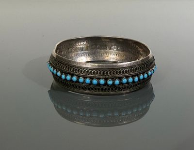 bague ornée de perles argentées et turquoise posée sur une surface réfléchissante