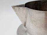 an old silver pitcher with a metal handle on a white surface