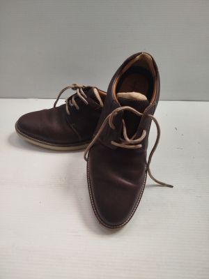 une paire de chaussures en cuir marron à lacets posée sur une surface blanche