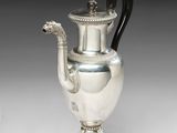 une cafetière ancienne en argent avec une poignée noire sur une surface blanche