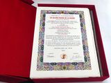 un livre ouvert accompagné d'un certificat, dans une boîte rouge posée sur une surface blanche