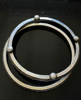 two silver bracelets on a black surface with a black background