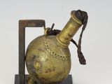 une petite bouteille en laiton munie d'une anse et posée sur un socle