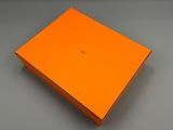 une boîte orange dont le couvercle est ouvert, posée sur une surface grise