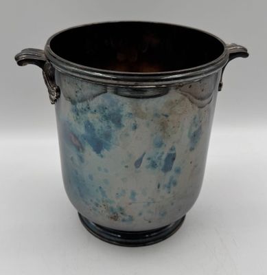 un vase en argent muni d'une anse, posé sur une surface blanche