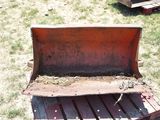 a red plow sitting in the grass next to a wooden bench