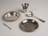 a silver plate with spoons, a silver cup, and a spoon