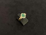 an image of a ring with a green stone on a black surface