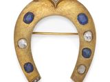 a close up of a gold horseshoe broochle with blue and white stones