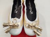une paire de chaussures blanches ornées de nœuds dorés, posée sur une boîte rouge