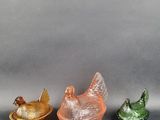 trois figurines en verre de couleurs différentes posées sur une surface grise