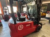 un chariot élévateur rouge garé dans un entrepôt, à côté d'autres véhicules