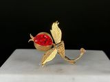 broche en forme de fleur plaquée or, ornée de cristaux rouges, sur un socle en marbre