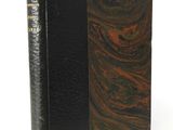 an old book with a black cover sitting on a white surface