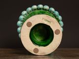 a green vase with beads on it sitting on a table