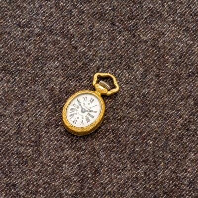 une petite montre de poche en or posée sur un tissu marron