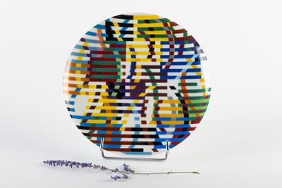 une assiette multicolore posée sur un socle orné d'une fleur
