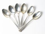 six cuillères en argent sont disposées en ligne sur une surface blanche