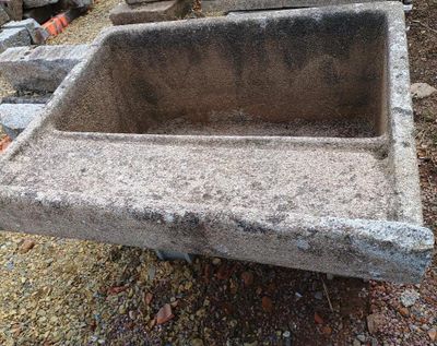 un évier en béton posé à même le sol, à côté d'un tas de pierres
