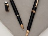 a black pen and a gold pen sitting on top of a piece of paper