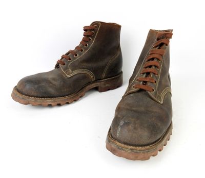 une paire de bottes marron avec des lacets marron, posées sur une surface blanche