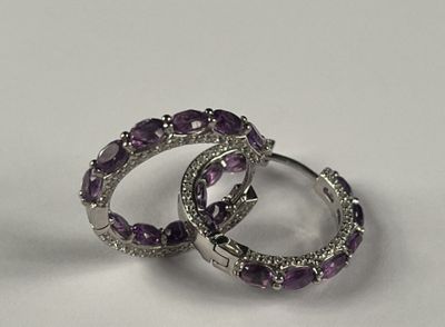 une paire de boucles d'oreilles créoles ornées de diamants violets et blancs, posées sur un fond blanc