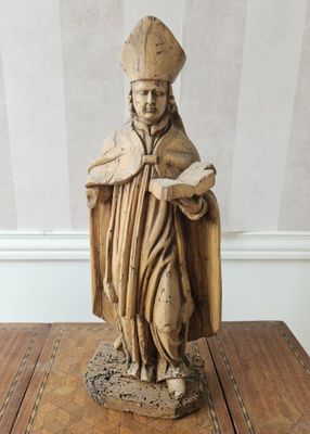 statue en bois représentant un homme tenant un livre posé sur une table en bois