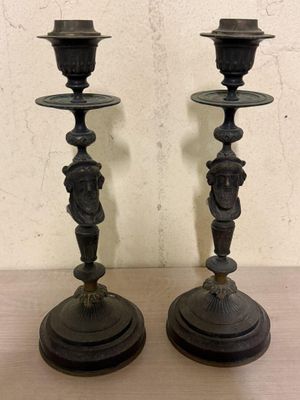 une paire de bougeoirs anciens noirs posés sur une table en bois, avec un mur en arrière-plan