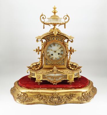 une horloge dorée posée sur un coussin rouge, sur une surface blanche