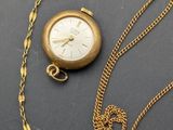 an image of a gold plated pocket watch and chain on a table