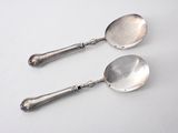 pair of silver spoons on a white surface with a white background