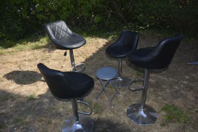 trois tabourets de bar en cuir noir posés dans l'herbe, à côté d'un buisson