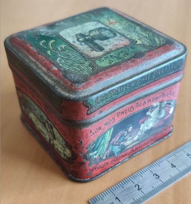 a small tin box with a picture on it next to a ruler