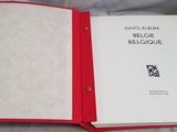 an open book with a red cover sitting on top of a bed