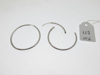 une paire de boucles d'oreilles créoles en argent posées sur une surface blanche, avec une étiquette de prix