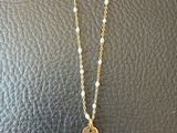 un collier en or avec une hamsa, des perles et une petite breloque en forme de hamsa