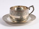 a silver cup and saucer sitting on a saucer