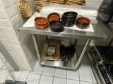 des casseroles et des poêles sont posées sur une table en acier inoxydable dans une cuisine