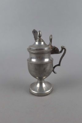 une théière ancienne en métal argenté, munie d'une anse et posée sur un socle