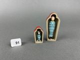 two miniature figurines of a woman and a cat in a coffin
