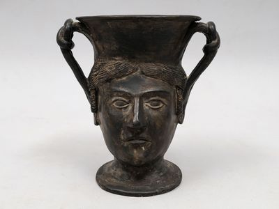 un vase noir orné d'un visage, posé sur une table