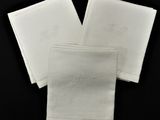 trois serviettes blanches ornées de monogrammes brodés sur fond noir