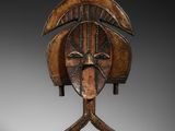 un masque en bois sur un support avec un fond noir