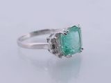 an emerald and diamond ring on a white surface