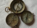 three antique brass compasses sitting on top of a white cloth
