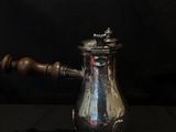 a silver coffee pot with a wooden handle on a black background