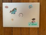 a white laptop with stickers on it on a wooden floor