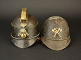 two helmets with gold decorations on them sitting on a black surface