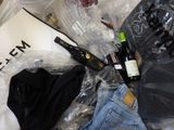 a pile of clothing and a bottle of wine on a bed