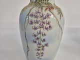a white vase with purple flowers on it on a white surface